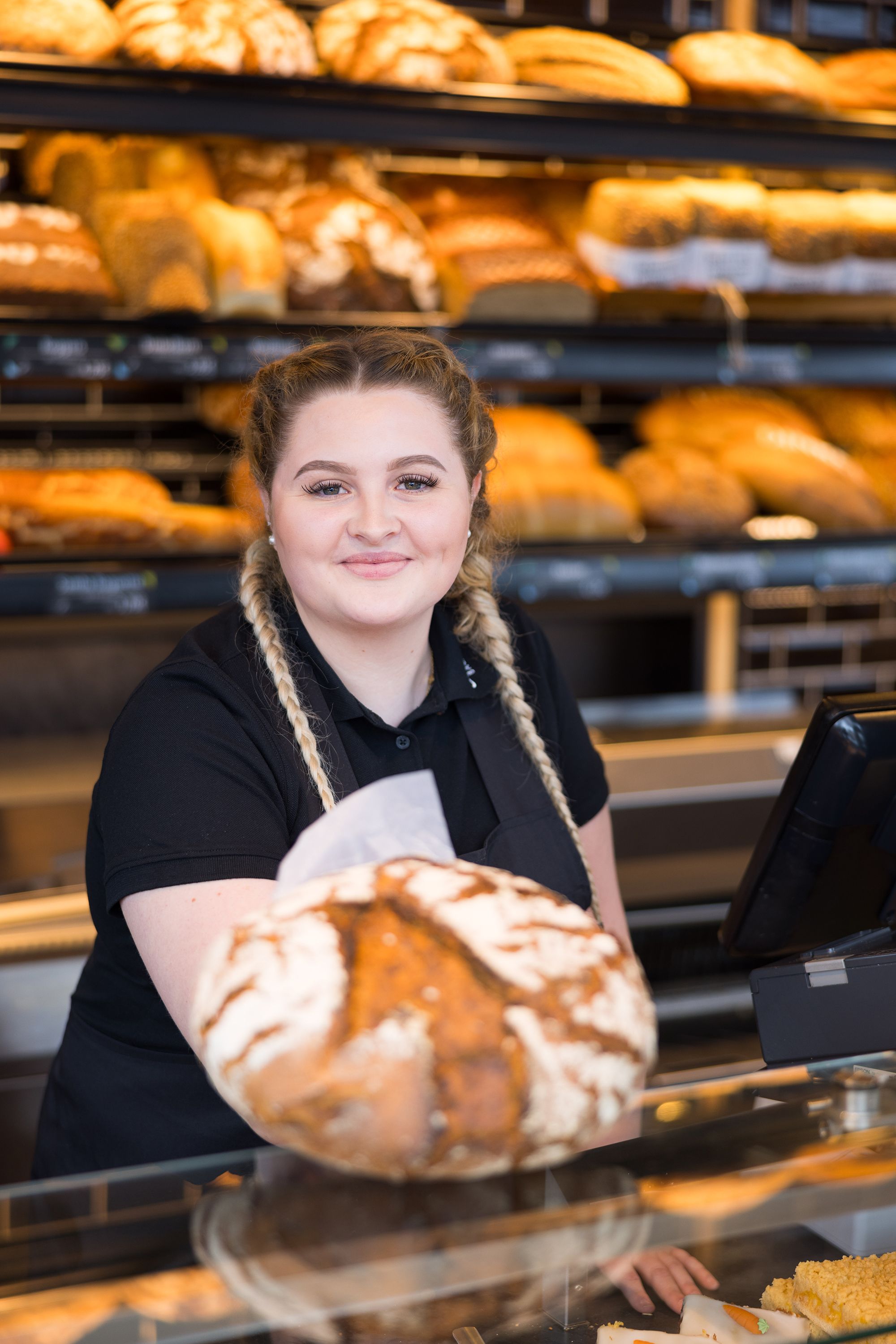 Verkäuferin der Bäckerei Schmidt reicht ein rundes Brot über die Theke.