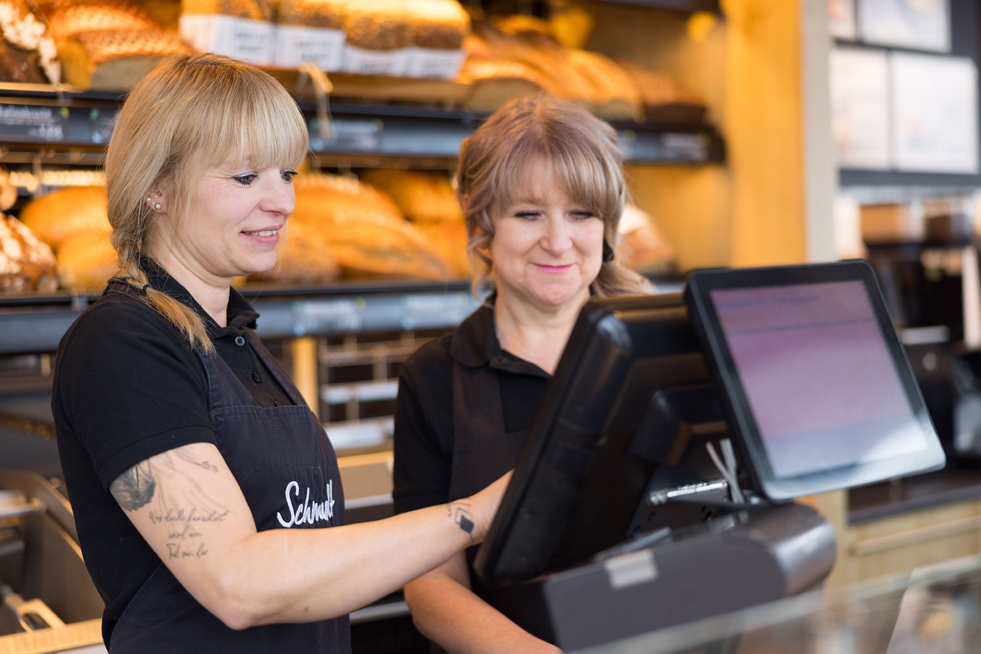Zwei Verkäuferinnen der Bäckerei Schmidt bedienen gemeinsam an der Kasse.