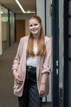Eine junge Frau lacht fröhlich in die Kamera. Sie steht im Gang der Büros