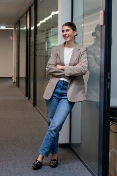 Eine junge Frau lehnt im Gang der Büros an der Wand und lächelt eine Kollegin an