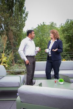 2 Kollegen, eine weiblich, einer männlich, tauschen sich bei gutem Wetter auf der Terrasse aus.