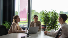 2 Studentinnen und ein Studenten unterhalten sich im Besprechungsraum. Sie sind gut gelaunt.