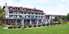 Großes Hotel mit rotem Dach, Sitzbereich mit blauen Sonnenschirmen und Garten davor.