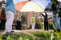 Auf dem Bild sind einige Senioren und eine Pflegekraft zu sehen, wie Sie eine bunte Plane in die Luft halten.