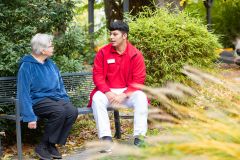 Ein Junger Mann sitzt mit einer Bewohnerin auf einer Bank im Park und unterhält sich