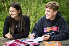 Zwei junge Leute sitzen nebeneinander und lachen. Vor ihnen liegen Unterlagen auf dem Tisch