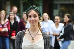 Eine Junge Frau steht vorne. Im Hintergrund sind weitere Personen zu sehen.