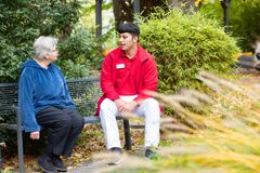 Ein junger Mann sitzt mit einer Bewohnerin auf einer Bank im Park und unterhält sich. 
