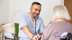 Ein Pflegefachmann hört mit einem Stethoskop eine Bewohnerin ab. 