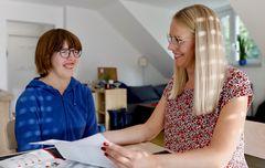 Eine Frau und ein Mädchen sitzen an einem Tisch, umgeben von Papieren und Notizen.