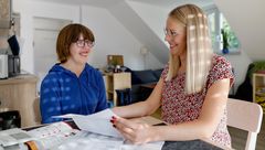 Eine Frau und ein Mädchen sitzen an einem Tisch, umgeben von Papieren und Notizen.