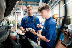 Zwei Kfz-Mechatroniker-Azubis überprüfen den Ölstand eines Fahrzeugs – ein praktischer Teil ihrer Ausbildung in der Fahrzeugwartung.