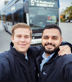 Zwei junge Männer, die sich in einem Selfie vor Bussen vom Stadtwerk Regensburg fotografieren.