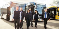 Ein Bild von mehreren Busfahrern, wie sie lächelnd vor den Bussen stehen bzw. gehen und in den Schicht starten .