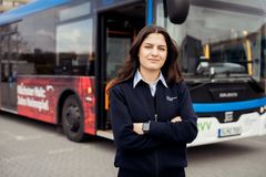 Eine angehende Fachkraft im Fahrbetrieb steht in Arbeitskleidung vor einem Bus und lächelt selbstbewusst in die Kamera. Das Bild vermittelt einen authentischen Einblick in die Ausbildung im Nahverkehr – mit Fokus auf Verantwortung, Technik und Teamspirit.