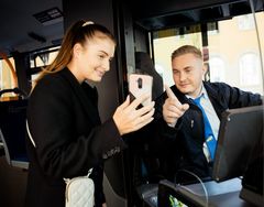 Ein Busfahrer wird im Bus angesprochen und zeigt der Kunden am Handy, wo der Bus hinfährt. 