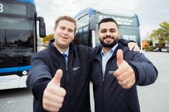 Zwei Busfahrer lächelnd vor seinen zwei Bussen vor Schichtbeginn. 