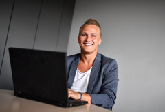 Mann im Sakko mit Laptop an einem Schreibtisch, freundlich blickend