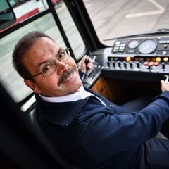 Bahnfahrer im Führerstand, Hand am Cockpit, lächelt in die Kamera