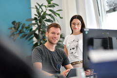 Zwei junge Menschen im Gespräch an einem Arbeitsplatz mit Computer