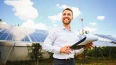 Mann mit Klemmbrett in der Hand und Solarpanel im Hintergrund