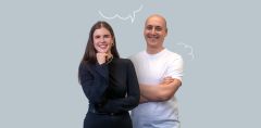 Eine lächelnde Frau mit schwarzem Oberteil und langen braunen Haaren steht neben einem  lächelnden Mann in weißem T-Shirt mit Glatze.