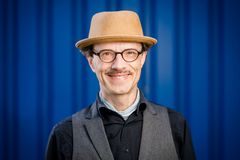 Ein Portrait eines Mannes mit Brille und Hut vor einem blauen HIntergrund, der bei der Stadt Elmshorn arbeitet steht vor 