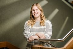 Eine junge Frau mit langen blonden Haaren und in einem gestreiften Pullover lehnt an einem Treppengeländer, die bei der Stadt Elmshorn arbeitet.  