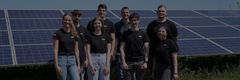 Eine Gruppe junger Menschen steht vor einem Solarpark. Sie tragen schwarze T-Shirts mit der Aufschrift "evm".