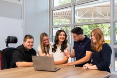 Drei junge Frauen und zwei junge Männer stehen an einem Tisch und schauen auf einen Computer