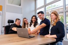 Zwei junge Männer und drei junge Frauen stehen an einem Tisch und schauen auf einen Bildschirm