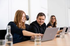 Zwei junge Frauen und ein junger Mann sitzen an einem Tisch und schauen auf einen Computer
