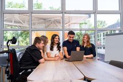 Mehrere junge Menschen stehen an einem Tisch und schauen auf einen Computer