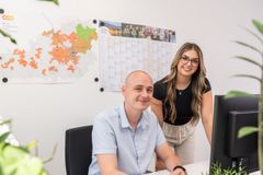 Ein junger Mann und eine junge Frau sitzen an einem Schreibtisch und lächeln freundlich