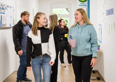 Sechs junge Menschen sind auf einem Flur paarweise im Gespräch.