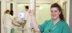 das Bild zeigt eine Pflegefachkraft mit Infusion Aufsteller in der Hand.