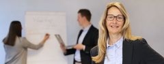 Das Bild zeigt eine Frau aus der Verwaltung mit einem Clipboard im Hintergrund.