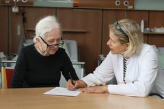 Das Bild zeigt eine ältere Frau und eine Ärztin, die zusammen am Tisch sitzen