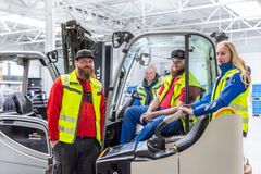 Mehrere Personen in Warnwesten arbeiten und kommunizieren zwischen Gabelstaplern in einer Lagerhalle – verdeutlicht den logistischen Arbeitsalltag.