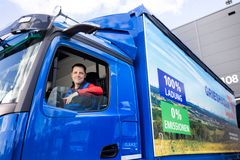 Lkw-Fahrer sitzt in der Kabine eines blauen Lkw mit der Aufschrift „100 % Logistik – 0 % Emission“ – steht für nachhaltige Speditionslösungen.