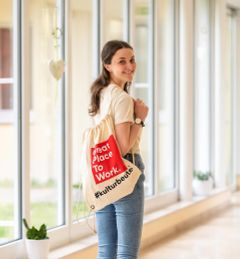 Lächelnde Person mit "Great Place to Work" Beutel dreht sich im Flur um.