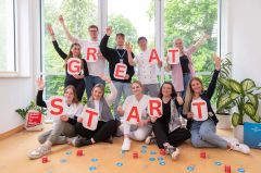 Gruppe junger Menschen hält "Great Start"-Buchstaben hoch und jubelt gemeinsam.