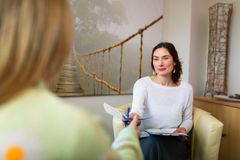 Therapeutin überreicht einer Patientin Unterlagen während eines persönlichen Gesprächs in einem freundlich gestalteten Therapieraum.