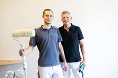 Zwei Haushandwerker lächelnd mit Malerwerkzeug in den Händen.