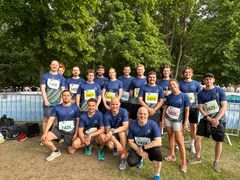 Eine Gruppe von Menschen steht in einem Park, gekleidet in blau-grüne Sportshirts mit Startnummer darauf zusammen und lächelt in die Kamera. 