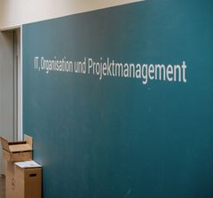 Wand mit Schriftzug IT, Organisation und Projektmanagement.