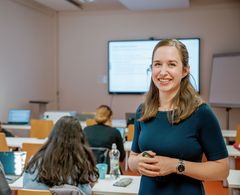 Eine Studentin steht vor anderen Student:innen der Fliedner Fachhochschule Düsseldorf und lächelt in die Kamera.