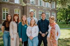 Ein Team aus der Verwaltung der Kaiserswerther Diakonie steht auf dem Campus und lächelt in die Kamera.