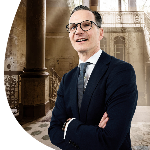 Enrico Ukrow, Geschäftsführer der Kliniken Beelitz, mit verschränkten Armen vor altem Klinikgebäude.