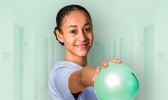 Auszubildende im Bereich Physiotherapie. Sie hält einen Ball in der Hand und steht in einem Krankenhausgang.